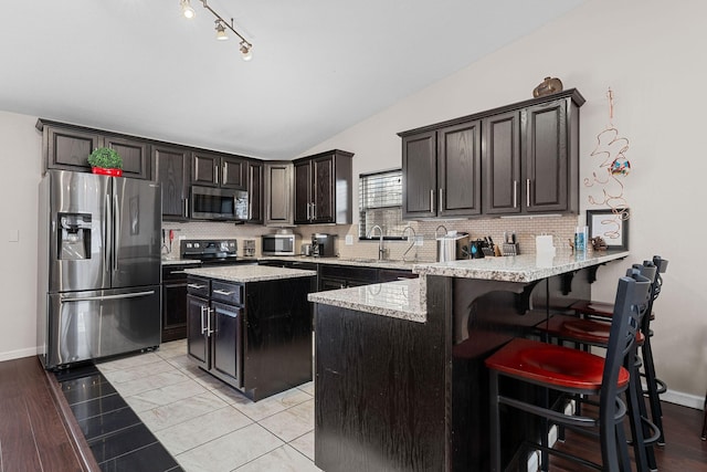 kitchen with lofted ceiling, a breakfast bar, tasteful backsplash, appliances with stainless steel finishes, and kitchen peninsula