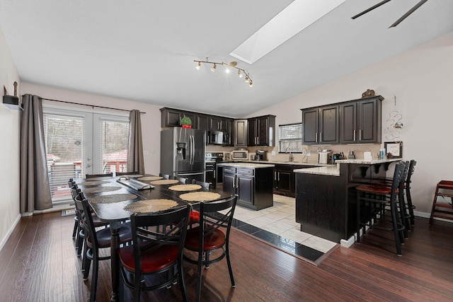 dining area featuring sink, light hardwood / wood-style flooring, lofted ceiling with skylight, and french doors