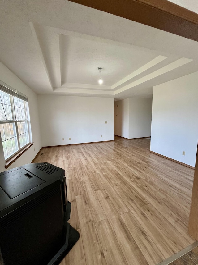 unfurnished living room featuring a raised ceiling, light hardwood / wood-style flooring, and a wood stove