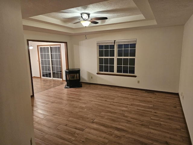 spare room with a wood stove, a textured ceiling, a raised ceiling, and wood finished floors