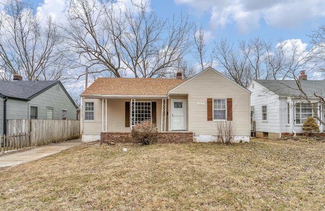 bungalow-style house featuring a shingled roof, a front yard, covered porch, and fence