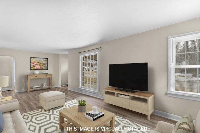 living room featuring a healthy amount of sunlight, baseboards, arched walkways, and wood finished floors