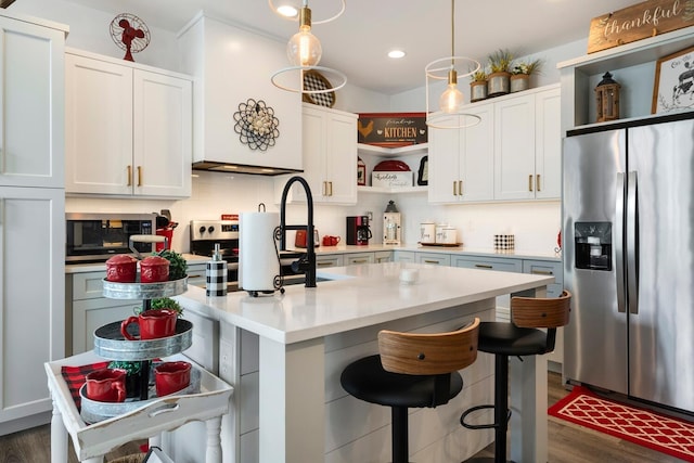 kitchen with stainless steel appliances, a center island with sink, white cabinets, and decorative light fixtures