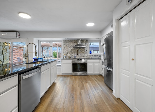 kitchen featuring sink, an AC wall unit, appliances with stainless steel finishes, wall chimney range hood, and white cabinets