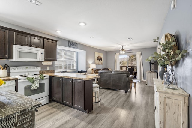 kitchen with dark brown cabinetry, light wood-type flooring, a kitchen breakfast bar, kitchen peninsula, and white appliances