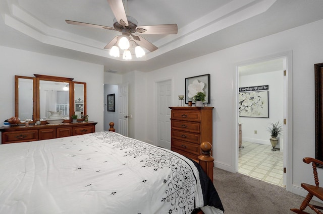 bedroom featuring a raised ceiling, carpet flooring, connected bathroom, and ceiling fan