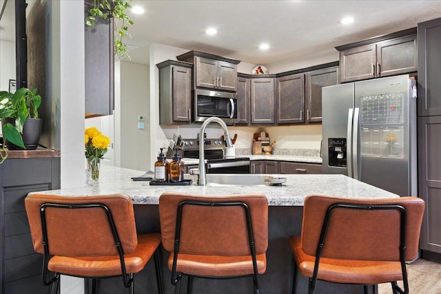kitchen featuring light stone counters, dark brown cabinetry, a breakfast bar area, and stainless steel appliances