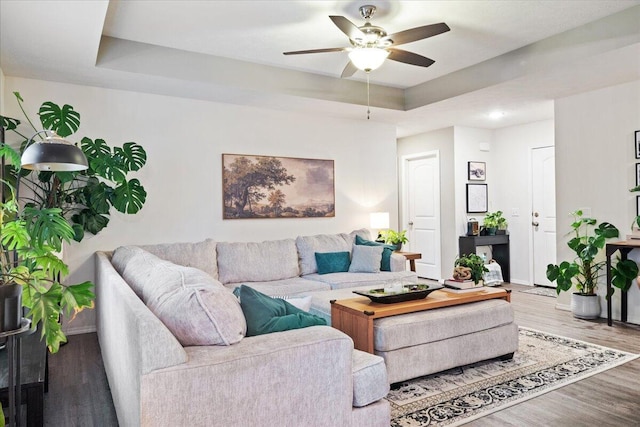 living area with a ceiling fan, a tray ceiling, wood finished floors, and baseboards