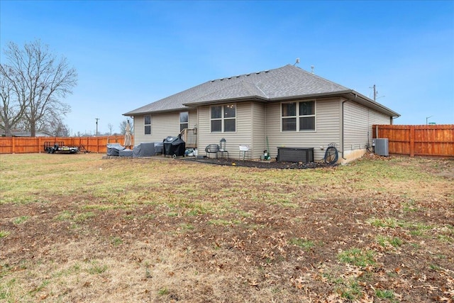 rear view of house with central air condition unit, a lawn, fence private yard, and roof with shingles