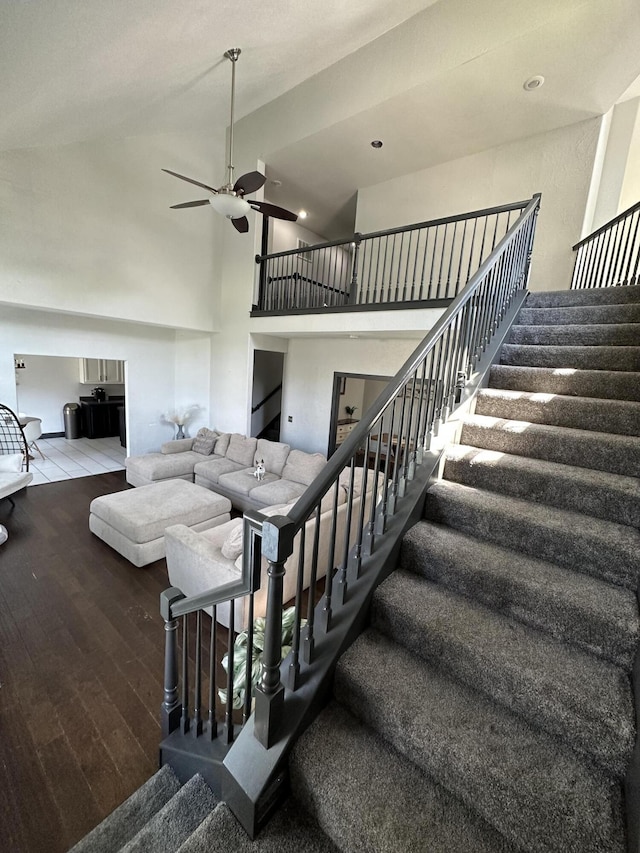 staircase with ceiling fan, hardwood / wood-style floors, and high vaulted ceiling