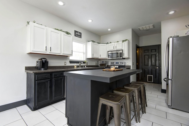 kitchen with appliances with stainless steel finishes, sink, white cabinets, a kitchen breakfast bar, and a center island