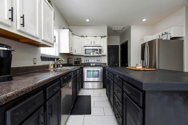 kitchen with appliances with stainless steel finishes, sink, light tile patterned floors, and white cabinets