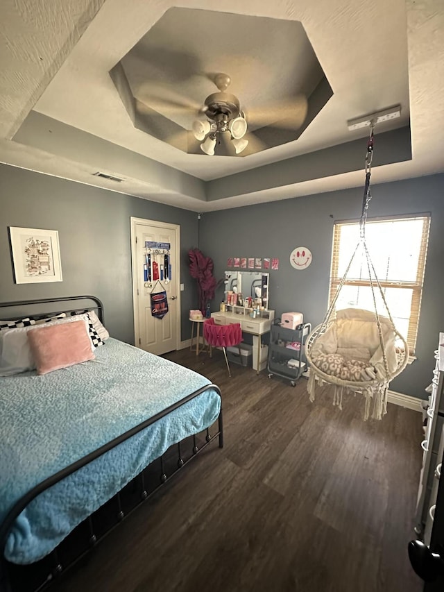 bedroom with dark hardwood / wood-style flooring, a tray ceiling, and ceiling fan