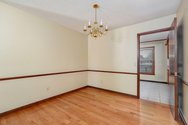 empty room with a notable chandelier, light hardwood / wood-style floors, and a textured ceiling