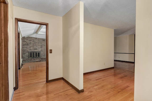 hallway with lofted ceiling with beams, a textured ceiling, and light hardwood / wood-style floors