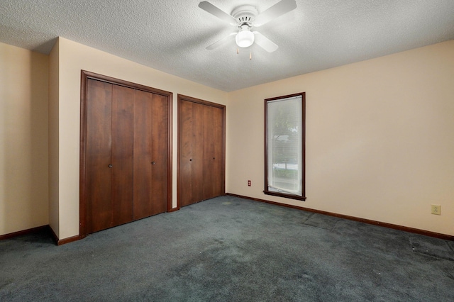 unfurnished bedroom with ceiling fan, two closets, a textured ceiling, and dark carpet