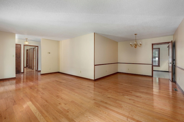 unfurnished room featuring a chandelier, a textured ceiling, and light wood-type flooring