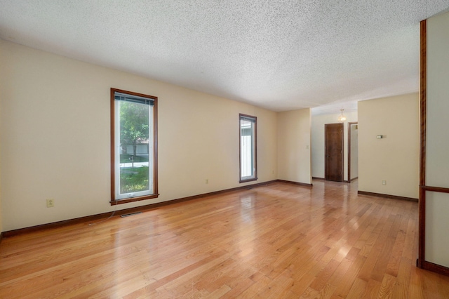 empty room with a textured ceiling and light hardwood / wood-style flooring