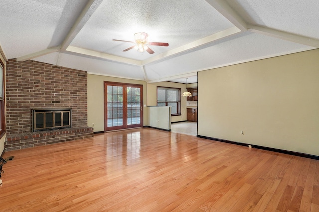 unfurnished living room featuring ceiling fan, lofted ceiling with beams, a textured ceiling, a brick fireplace, and light wood-type flooring