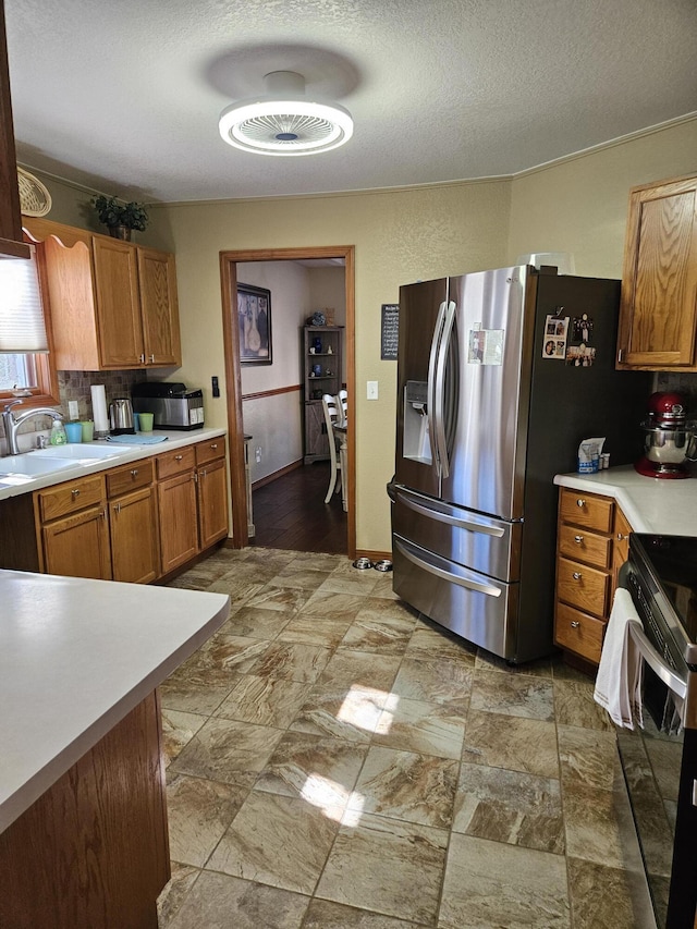 kitchen with stainless steel refrigerator with ice dispenser, sink, a textured ceiling, and electric stove