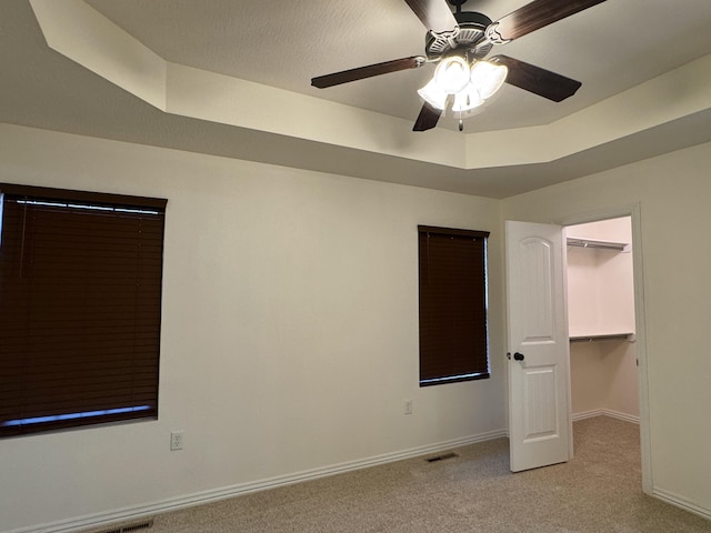 unfurnished bedroom with ceiling fan, a raised ceiling, light carpet, a spacious closet, and a closet