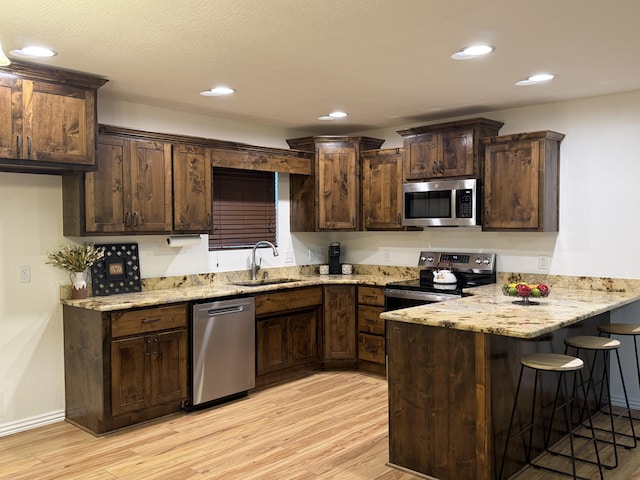 kitchen featuring light stone counters, sink, light wood-type flooring, and appliances with stainless steel finishes