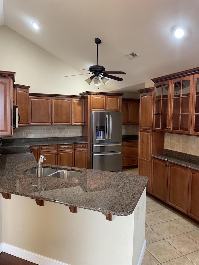 kitchen featuring vaulted ceiling, a kitchen bar, decorative backsplash, light tile patterned floors, and stainless steel appliances