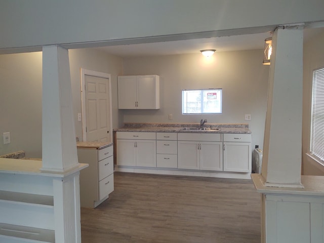 kitchen with light hardwood / wood-style floors, sink, decorative columns, and white cabinets