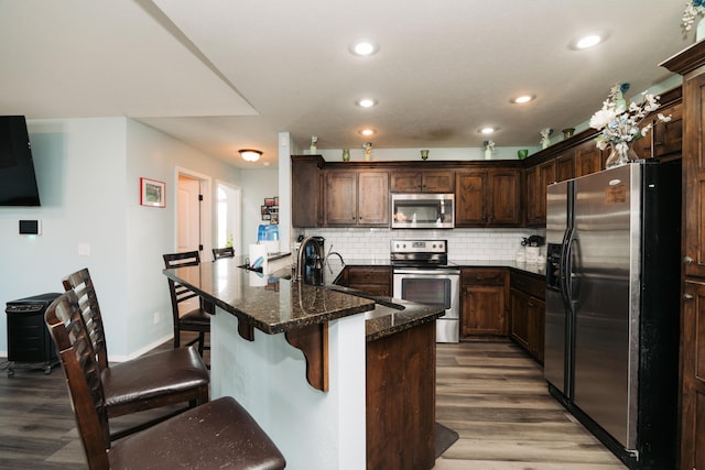 kitchen featuring sink, backsplash, dark stone counters, appliances with stainless steel finishes, and a kitchen breakfast bar