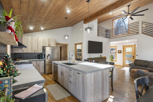 kitchen featuring stainless steel appliances, open floor plan, a sink, and light brown cabinetry