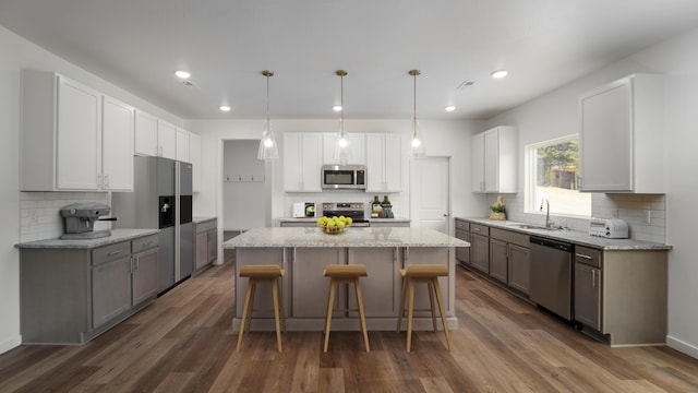 kitchen featuring appliances with stainless steel finishes, sink, white cabinetry, a kitchen island, and decorative light fixtures