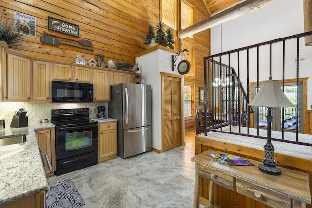 kitchen with a towering ceiling, black appliances, wood walls, light stone counters, and decorative backsplash