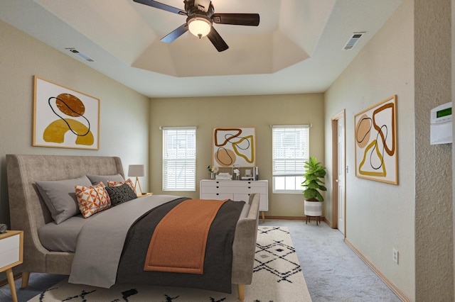 bedroom featuring a tray ceiling, ceiling fan, multiple windows, and light carpet