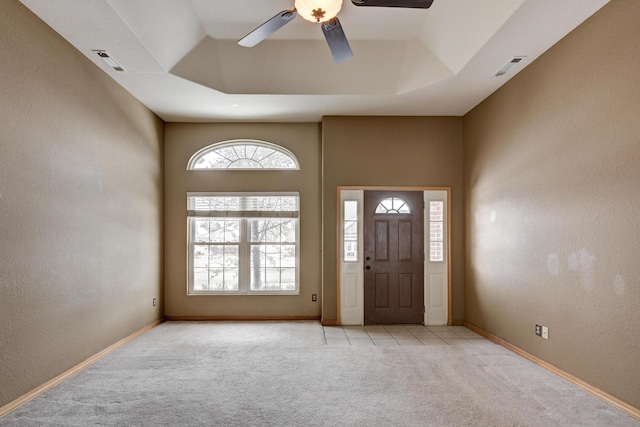 entrance foyer with a raised ceiling, ceiling fan, and light colored carpet