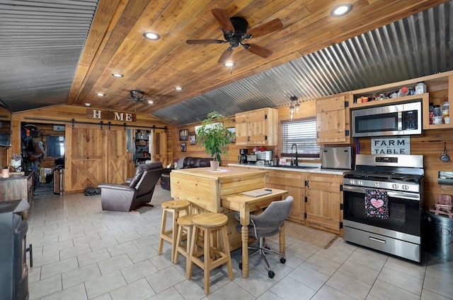 kitchen featuring appliances with stainless steel finishes, wooden walls, lofted ceiling, a barn door, and sink