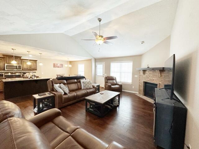 living room with vaulted ceiling, ceiling fan, dark hardwood / wood-style floors, and a fireplace