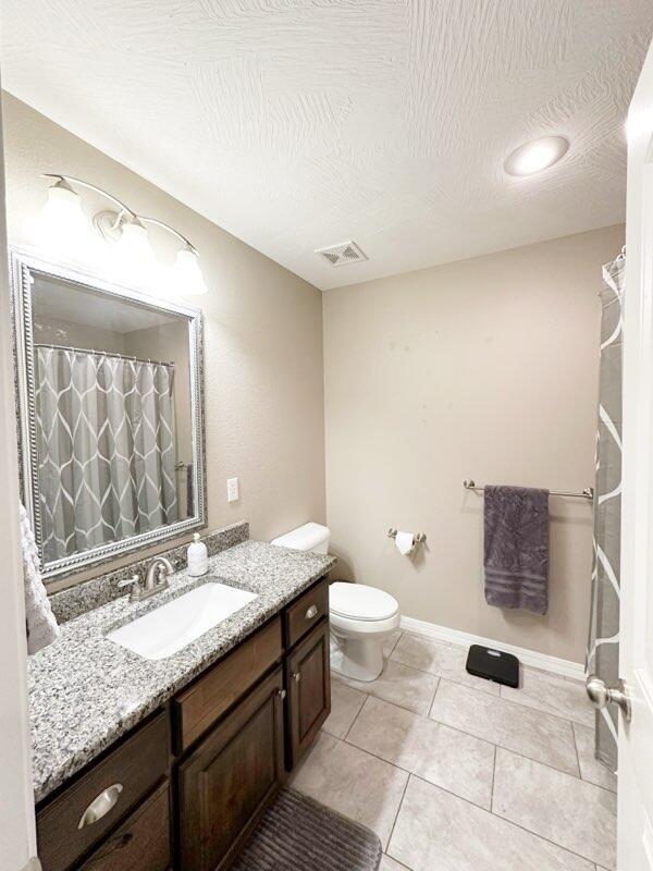 bathroom with toilet, a textured ceiling, tile patterned flooring, and vanity