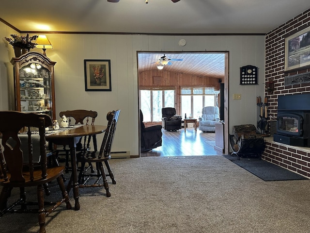 dining area with a wood stove, baseboard heating, ornamental molding, ceiling fan, and carpet flooring