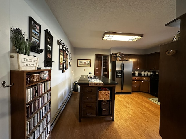 kitchen with baseboard heating, dishwasher, light wood finished floors, dark countertops, and stainless steel fridge