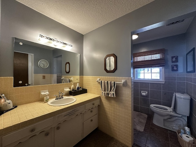 bathroom with a wainscoted wall, tile walls, toilet, a textured ceiling, and tile patterned flooring
