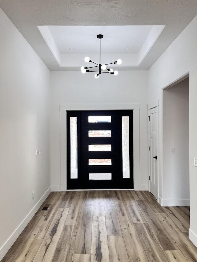 foyer featuring a tray ceiling, a chandelier, and light wood-type flooring