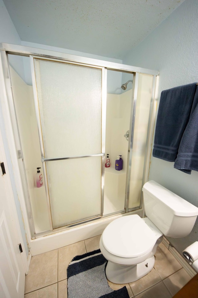 bathroom with a textured ceiling, a shower with door, toilet, and tile patterned floors