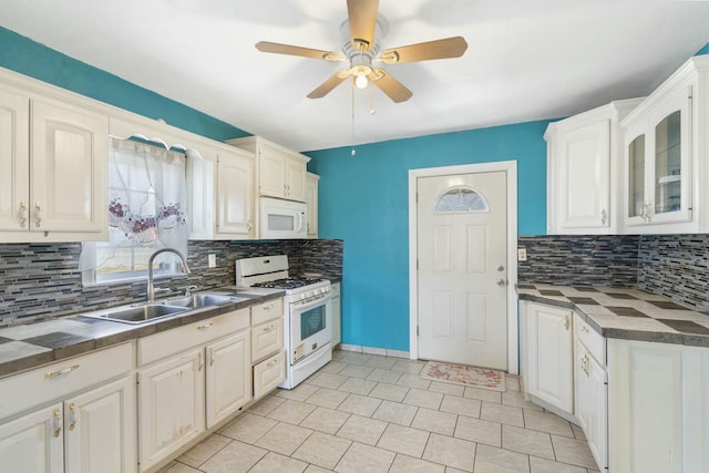 kitchen featuring dark countertops, glass insert cabinets, white cabinetry, a sink, and white appliances