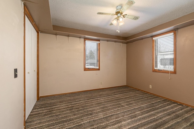 spare room with a textured ceiling, dark colored carpet, and ceiling fan