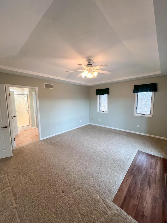 empty room with a raised ceiling, ceiling fan, and carpet flooring