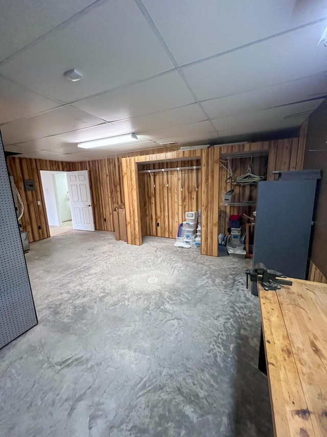 basement featuring a paneled ceiling and wood walls