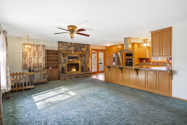 unfurnished living room featuring ceiling fan, dark colored carpet, and a stone fireplace