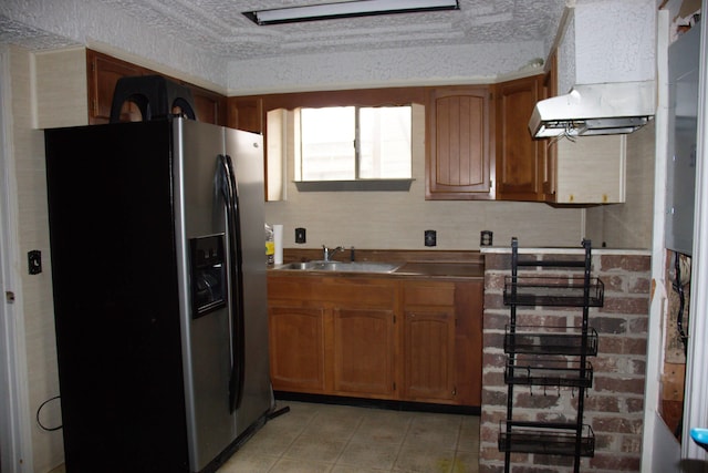 kitchen featuring a sink, light countertops, brown cabinetry, and stainless steel fridge