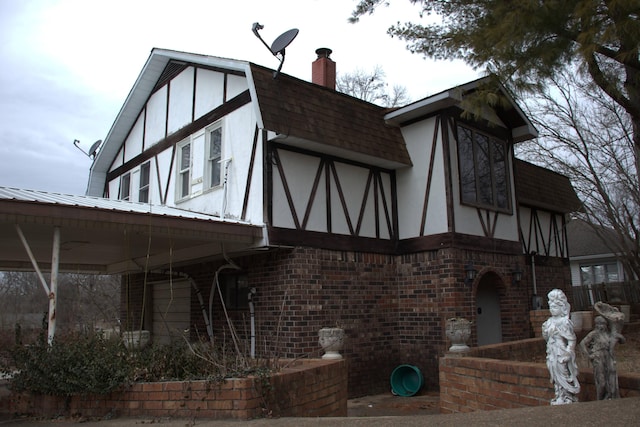 view of front of home featuring brick siding, a chimney, stucco siding, a shingled roof, and a gambrel roof