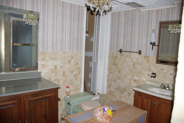 bathroom featuring toilet, a sink, tile walls, wallpapered walls, and an inviting chandelier